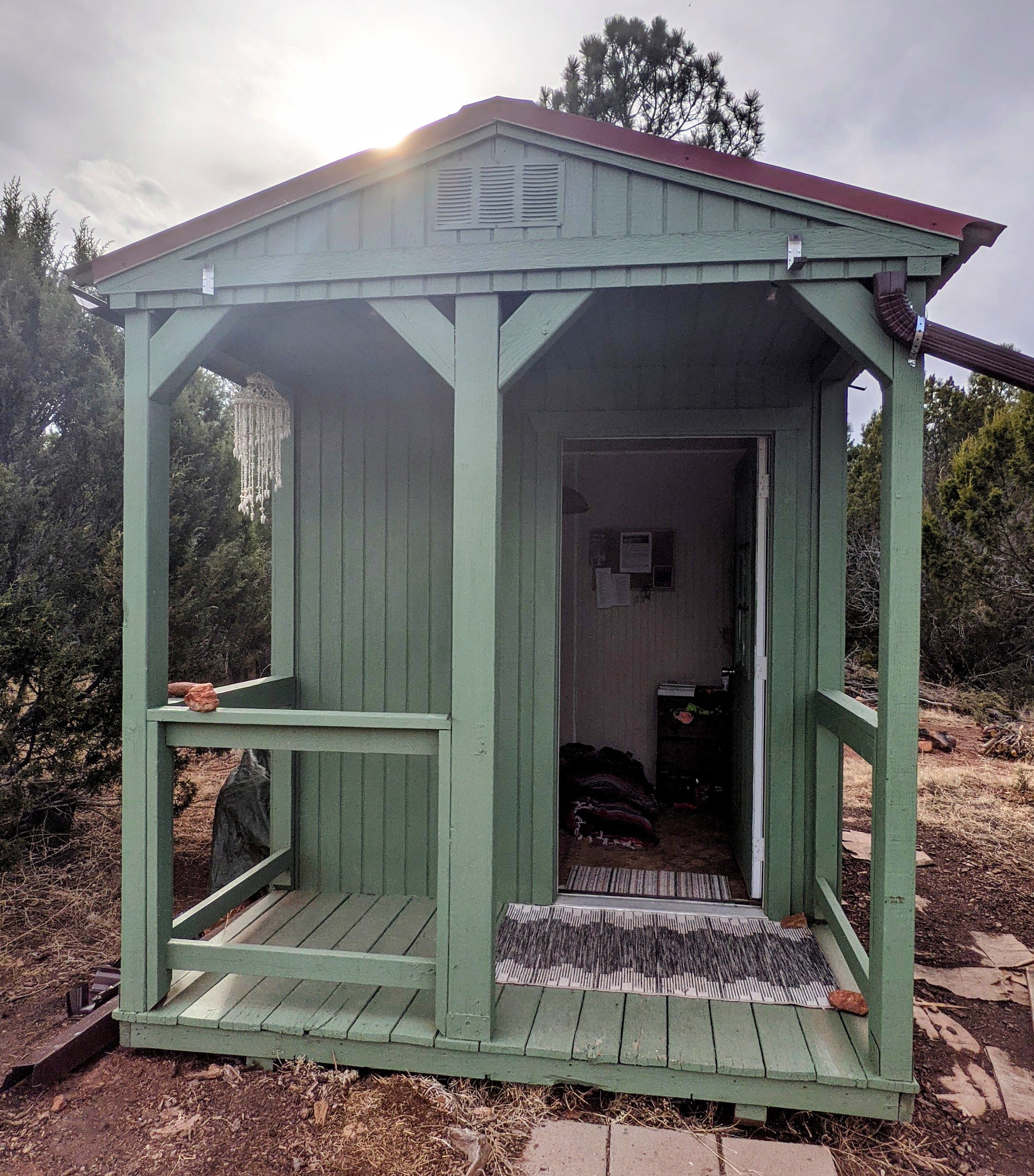 a single roomed green cabin with a small front porch